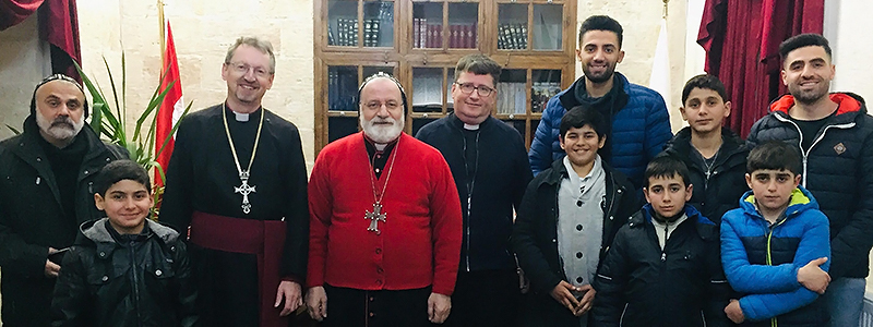 A photograph of Bishop Robert, Clergy Members, and young school children.