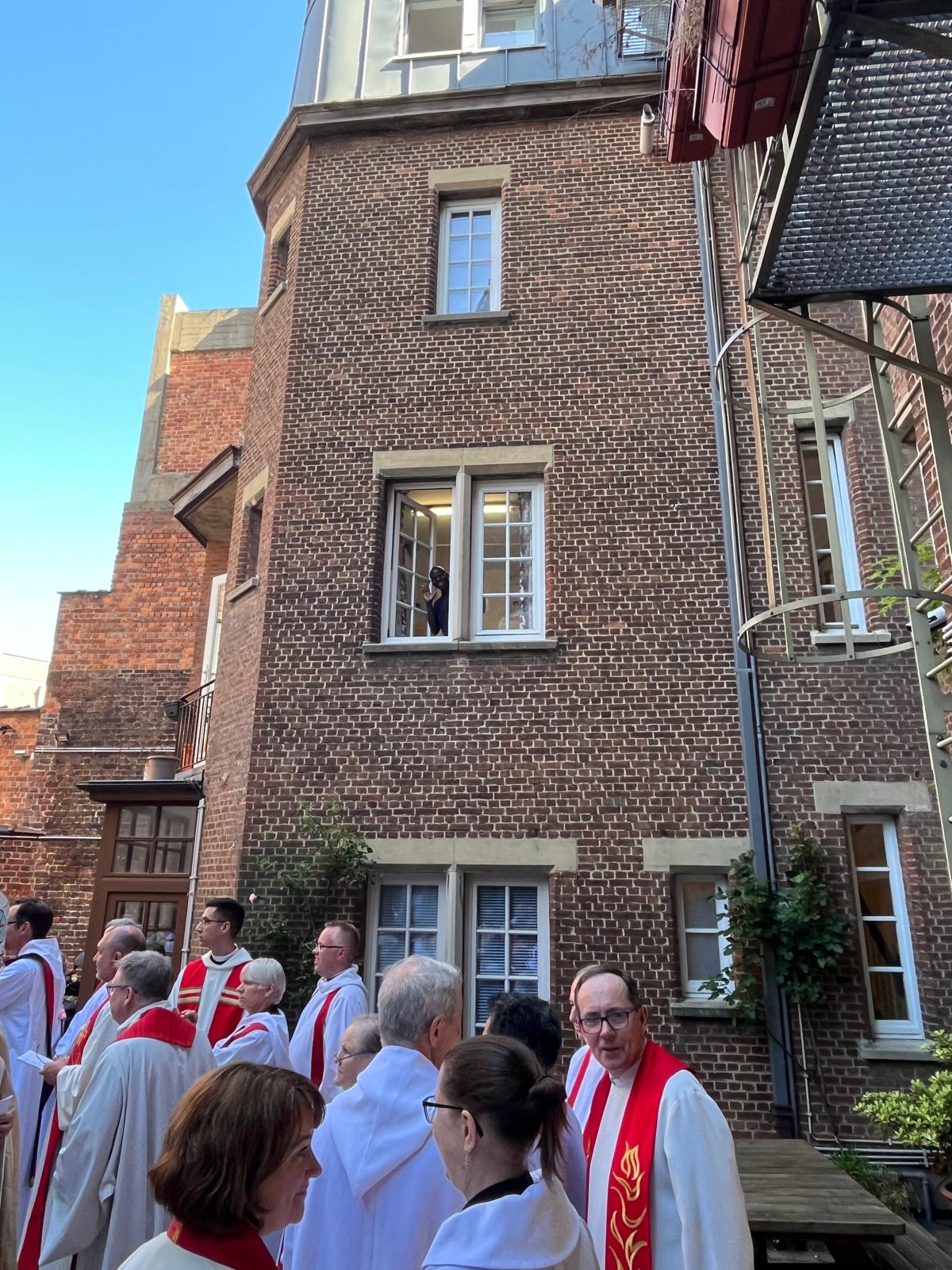 A man waves from a window to a group of clergy