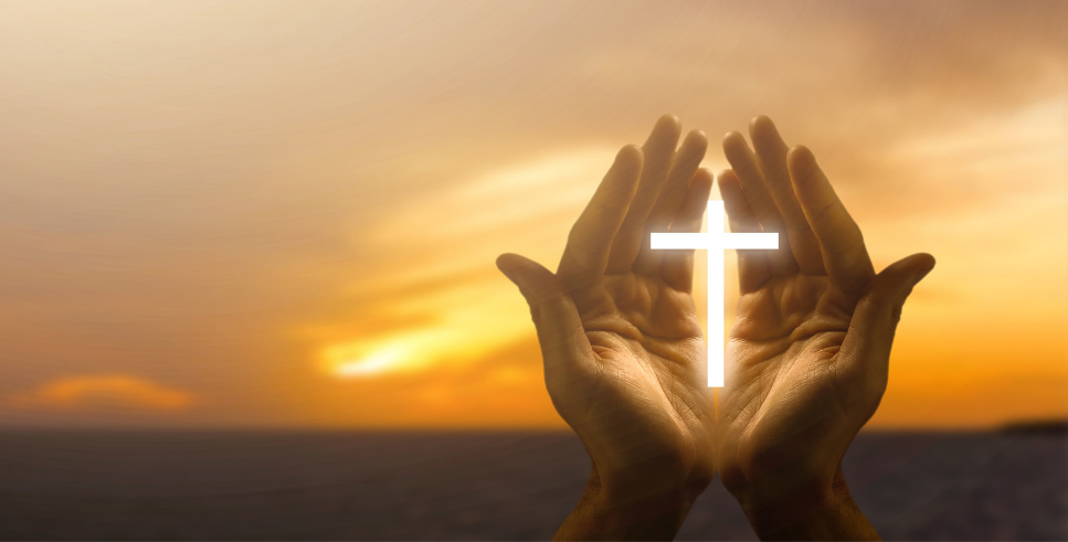 hands holding a light cross against a sunset