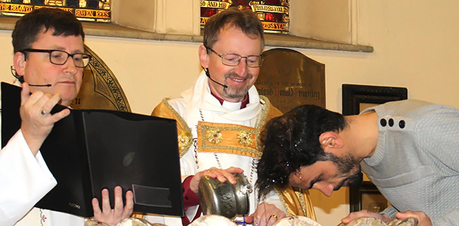 Bishop Robert performing a baptism whilst beaming with joy.