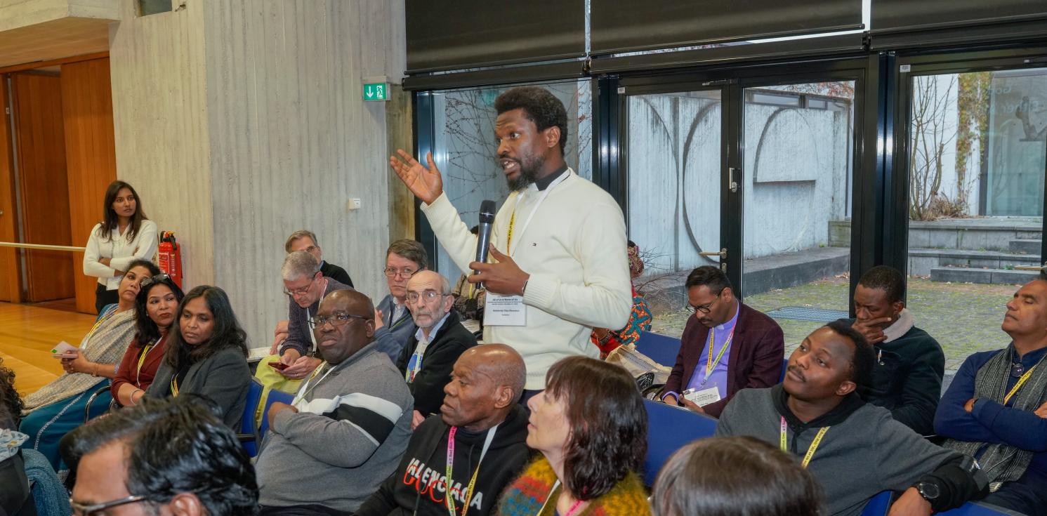 A man stands up to speak amidst others at a conference