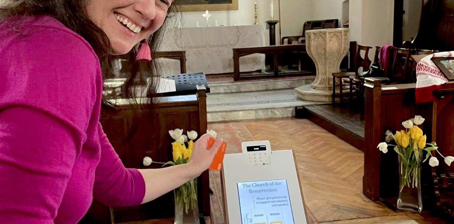 A lady smiles to camera while using a digital giving machine