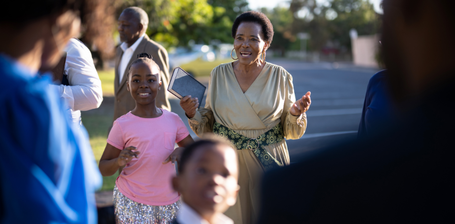 People talking with an adult lady holding her arms out and smiling next to a child