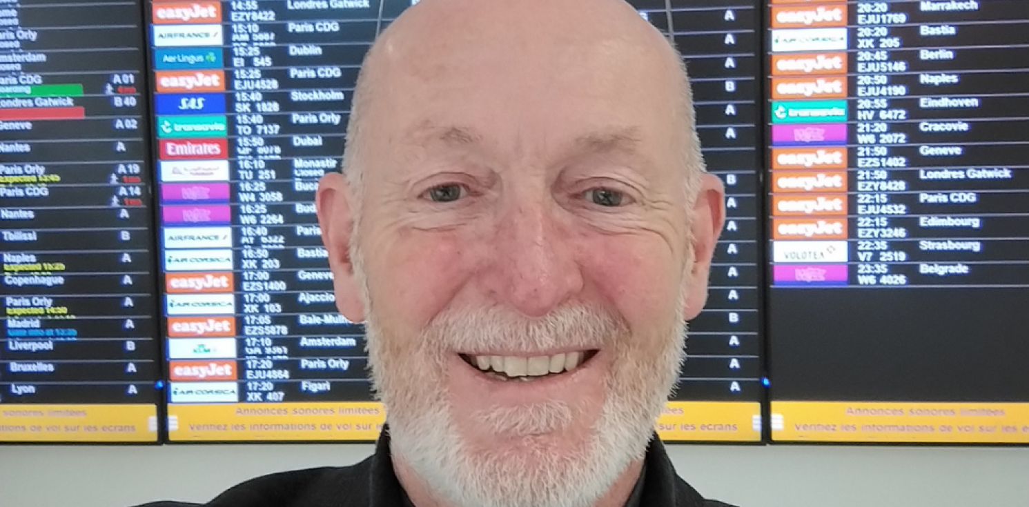 a man faces the camera in front of an airport board