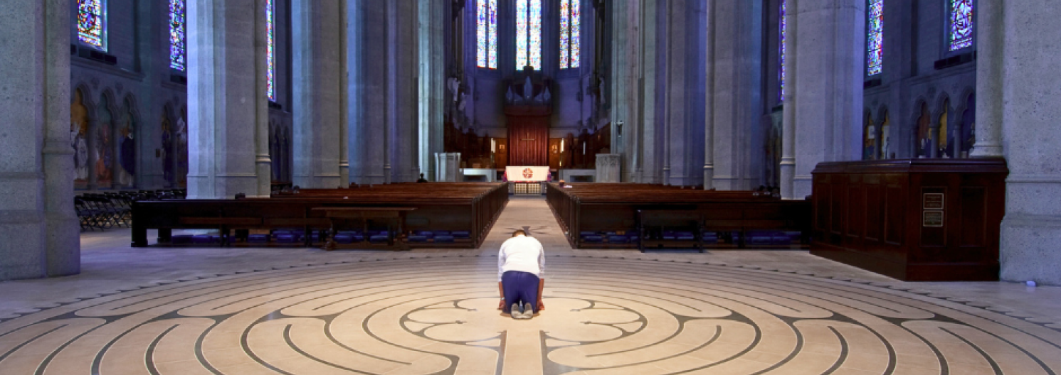 A man kneels in prayer in an empty church with a labyrinth on the floor