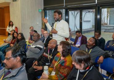 A man stands up to speak amidst others at a conference