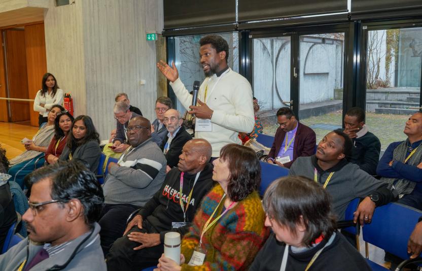 A man stands up to speak amidst others at a conference
