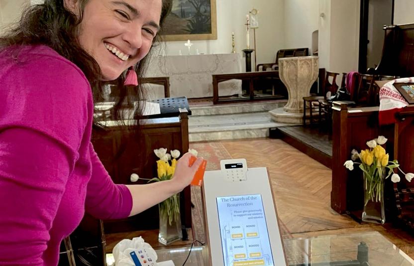 A lady smiles to camera while using a digital giving machine
