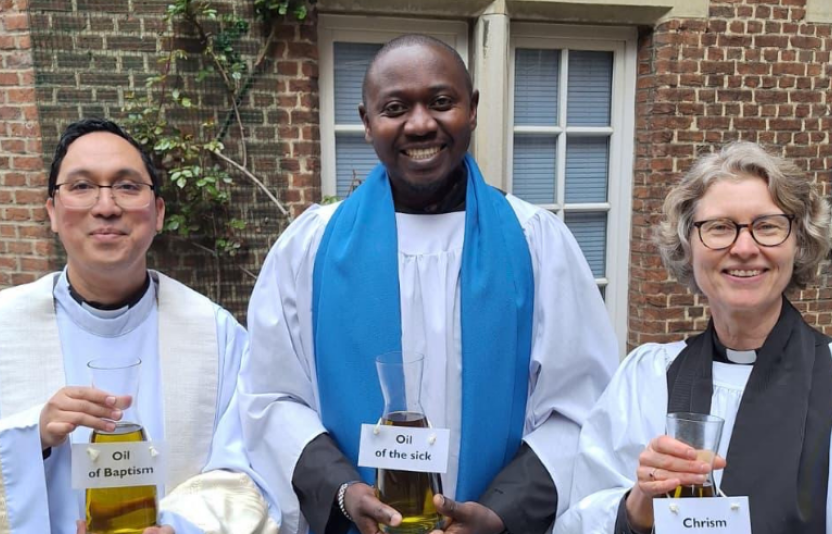 three clergy in a row looking to camera holding Chrism vials