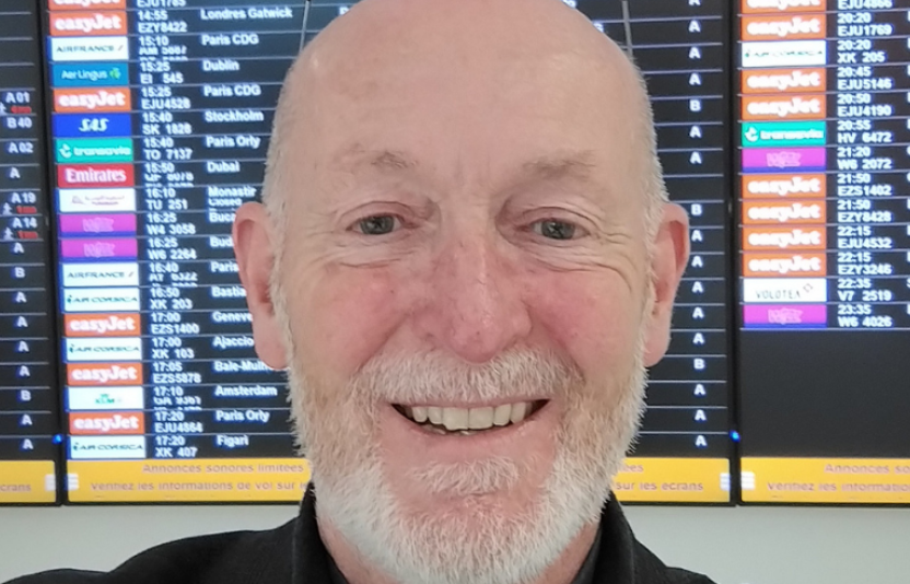 a man faces the camera in front of an airport board