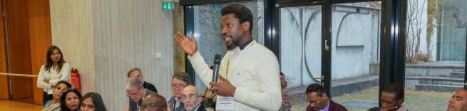 A man stands up to speak amidst others at a conference