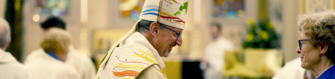 Bishop Robert reaching out to shake hands with a lady in a blue coat in church