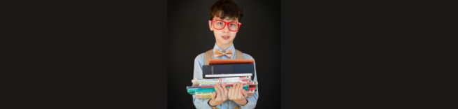 boy holding a pile of books against a black background