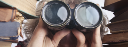 A lady with binoculars stares between piles of books