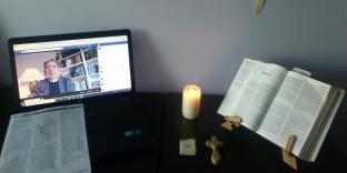 A table containing a candle, an open bible, and an online video service.