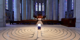 A man kneels in prayer in an empty church with a labyrinth on the floor