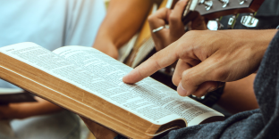 Open bible with someone pointing to a verse