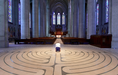 A man kneels in prayer in an empty church with a labyrinth on the floor