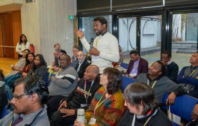 A man stands up to speak amidst others at a conference