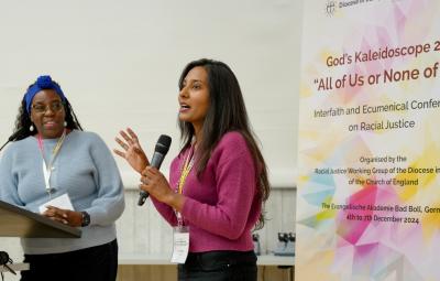 Young person speaking next to a banner of the racial justice conference and holding a mic