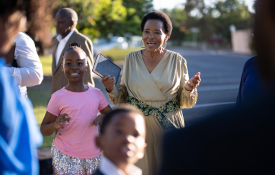 People talking with an adult lady holding her arms out and smiling next to a child