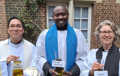 three clergy in a row looking to camera holding Chrism vials