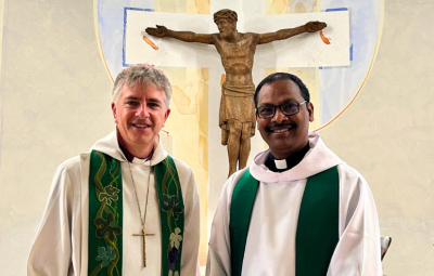 Two clergy face camera and smile inside a church
