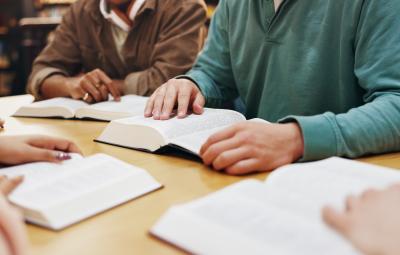 a table with people sat around, just the hands visible and with open books