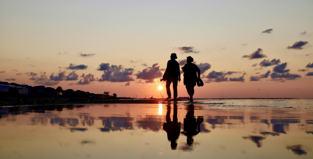 two people silhouetted against the sunset walking on a beach